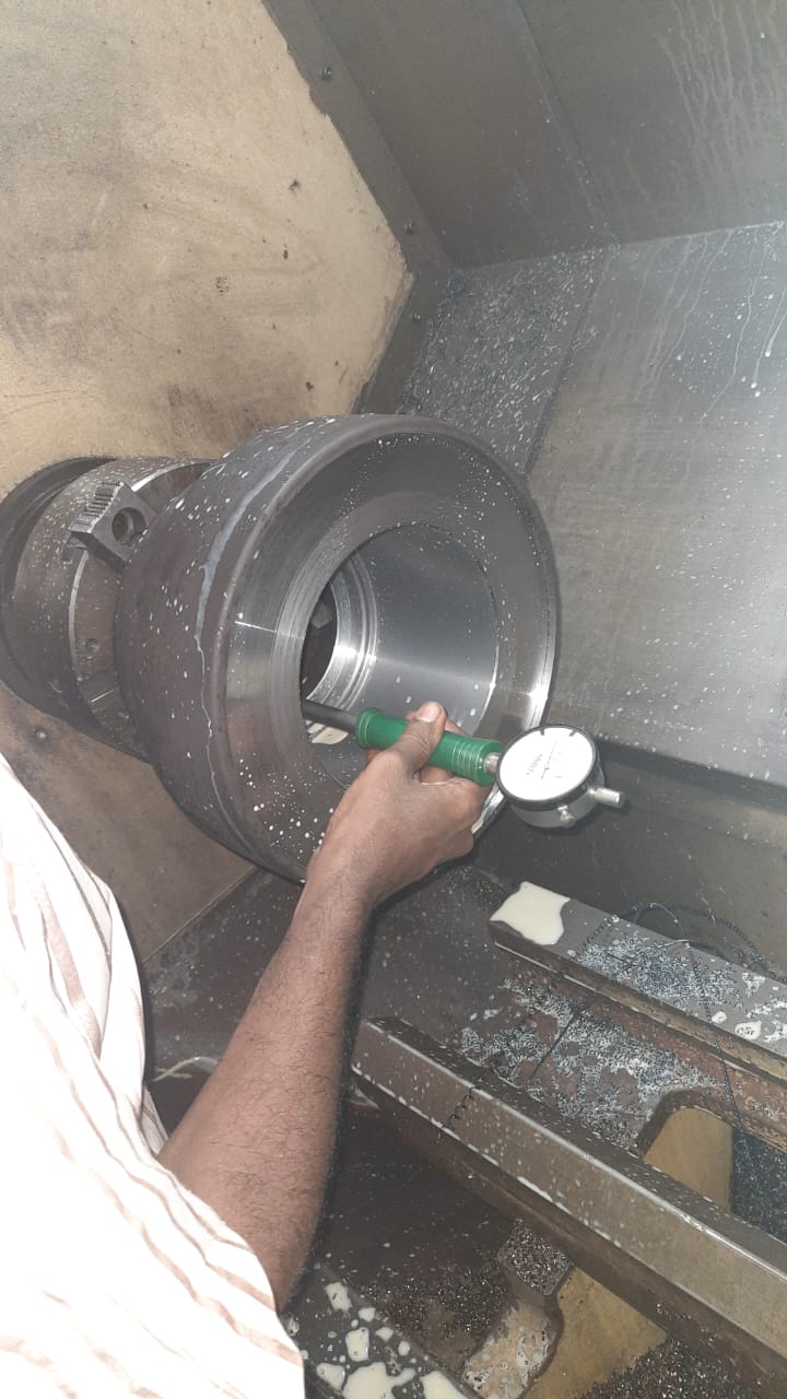Machinist using a dial bore gauge to measure the internal diameter of a large cylindrical part on a lathe