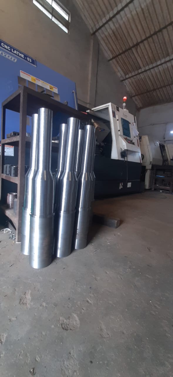 Large stepped shafts standing on a workshop floor next to a CNC lathe machine