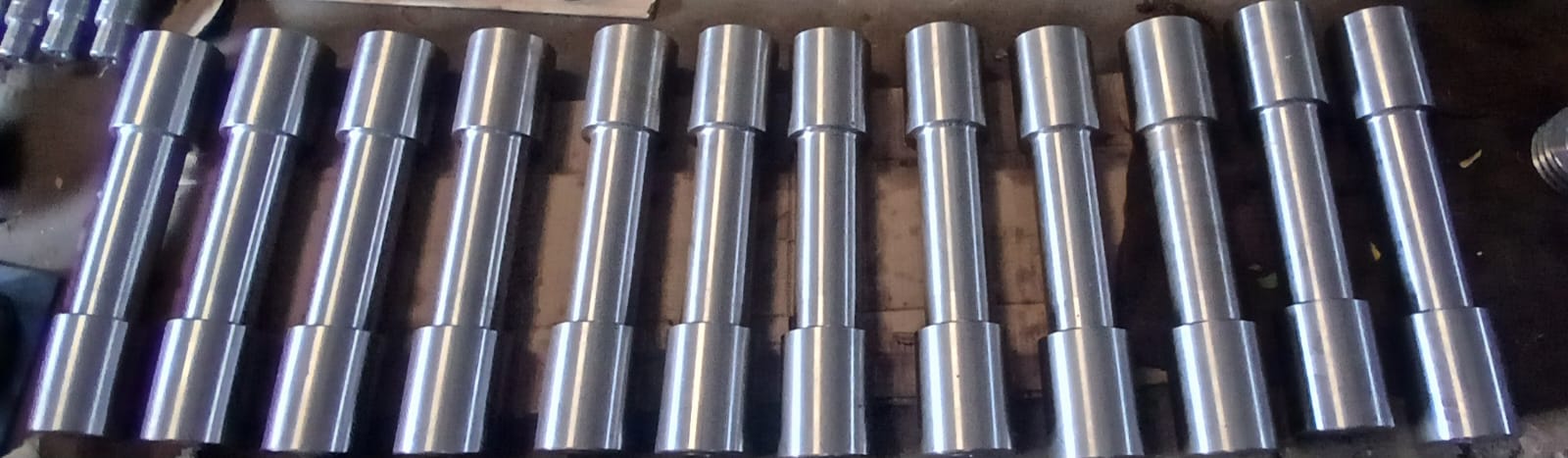 Horizontal row of identical precision-turned metal pins with center grooves