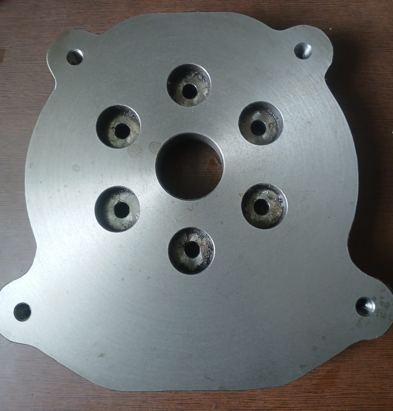 Flat machined metal plate with a central hole and a circular pattern of six smaller holes