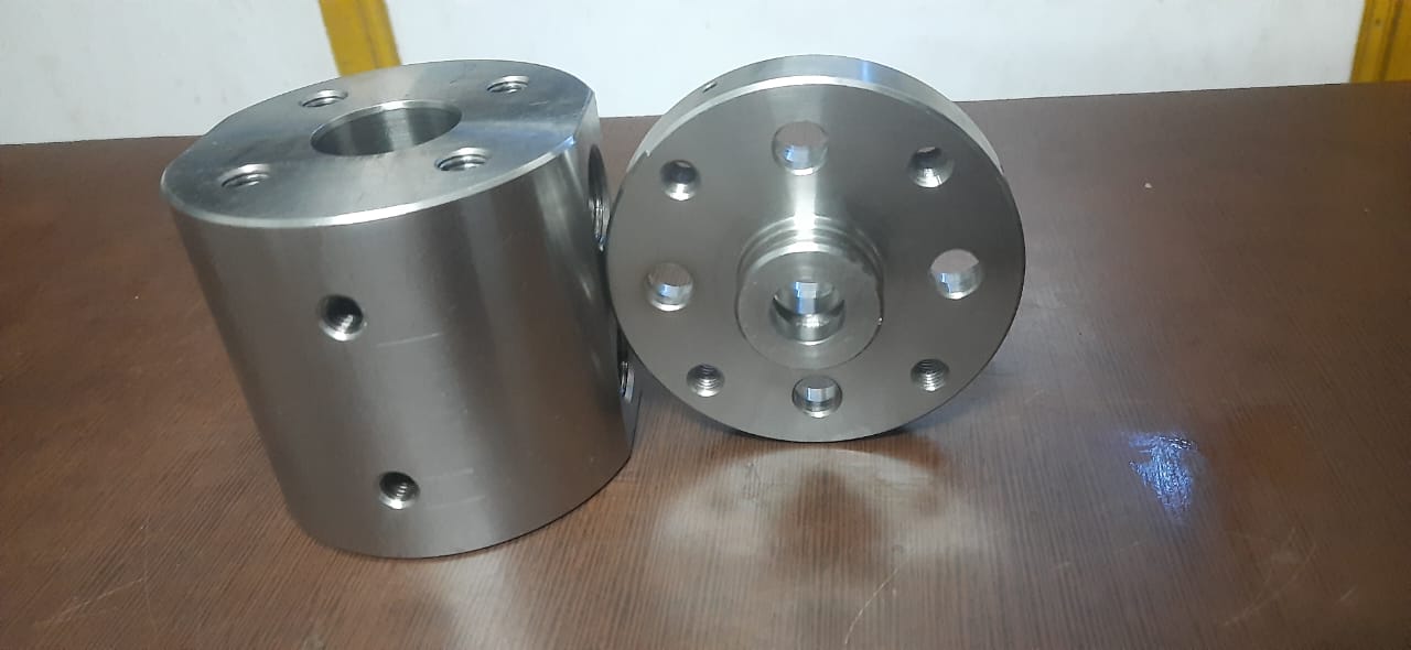 Two different precision-turned cylindrical parts with hole patterns on a wooden surface