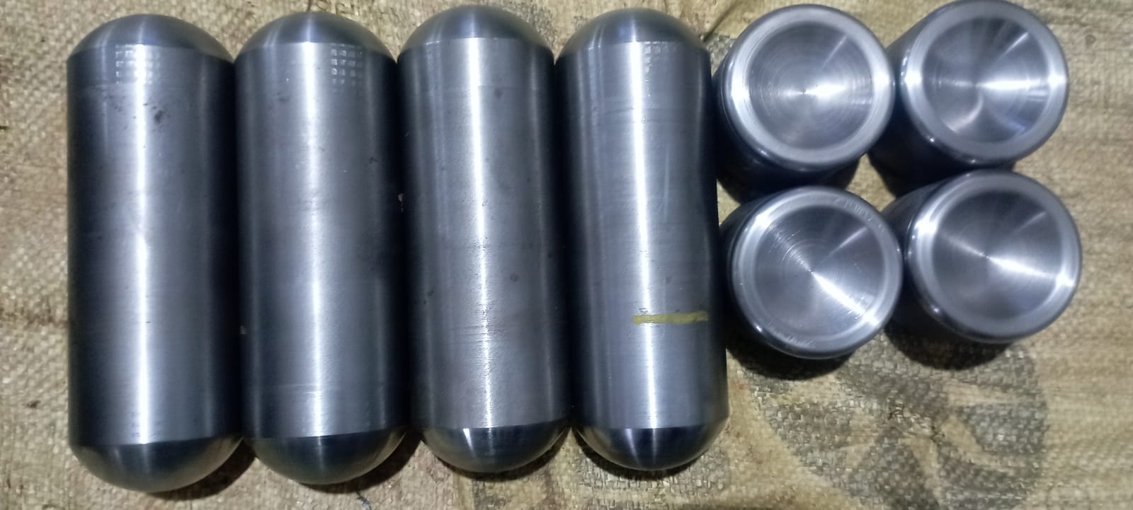 A collection of cylindrical metal slugs with rounded ends and several shorter precision-faced steel caps